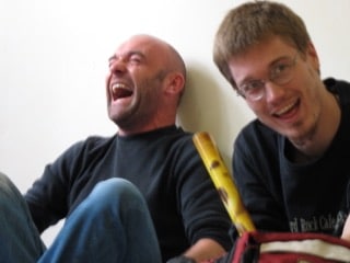 Deux personnes assises contre un mur en train de rire sincèrement, illustrant la joie spontanée et la complicité humaine dans le rire partagé.